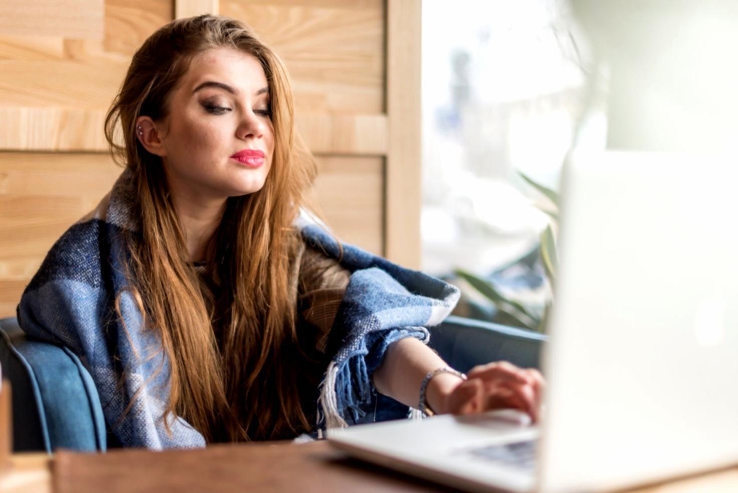 Student reviewing financial analysis materials on laptop with notes and charts spread across desk